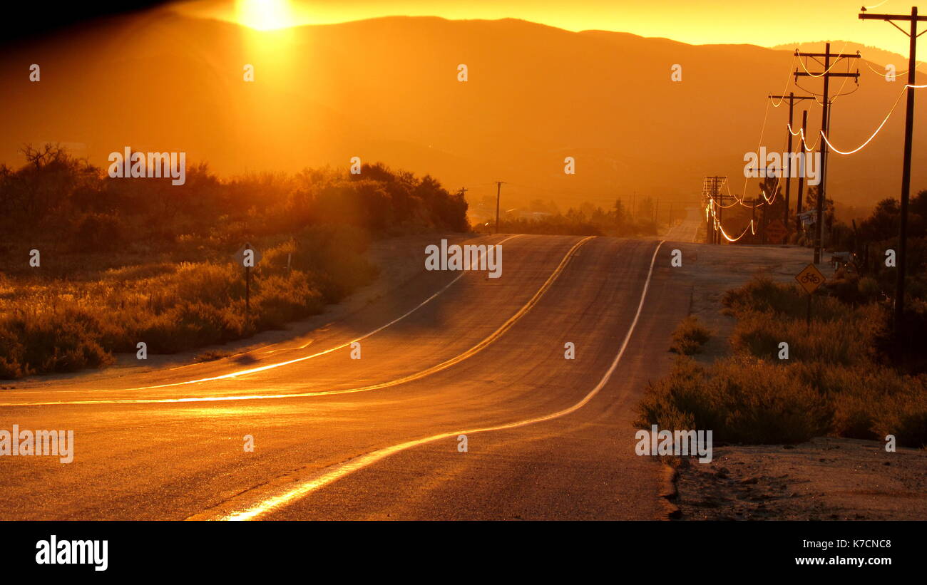 Curva desert highway road che va pensato il Southern California golden state al tramonto con una linea telefonica glinting con oro Foto Stock