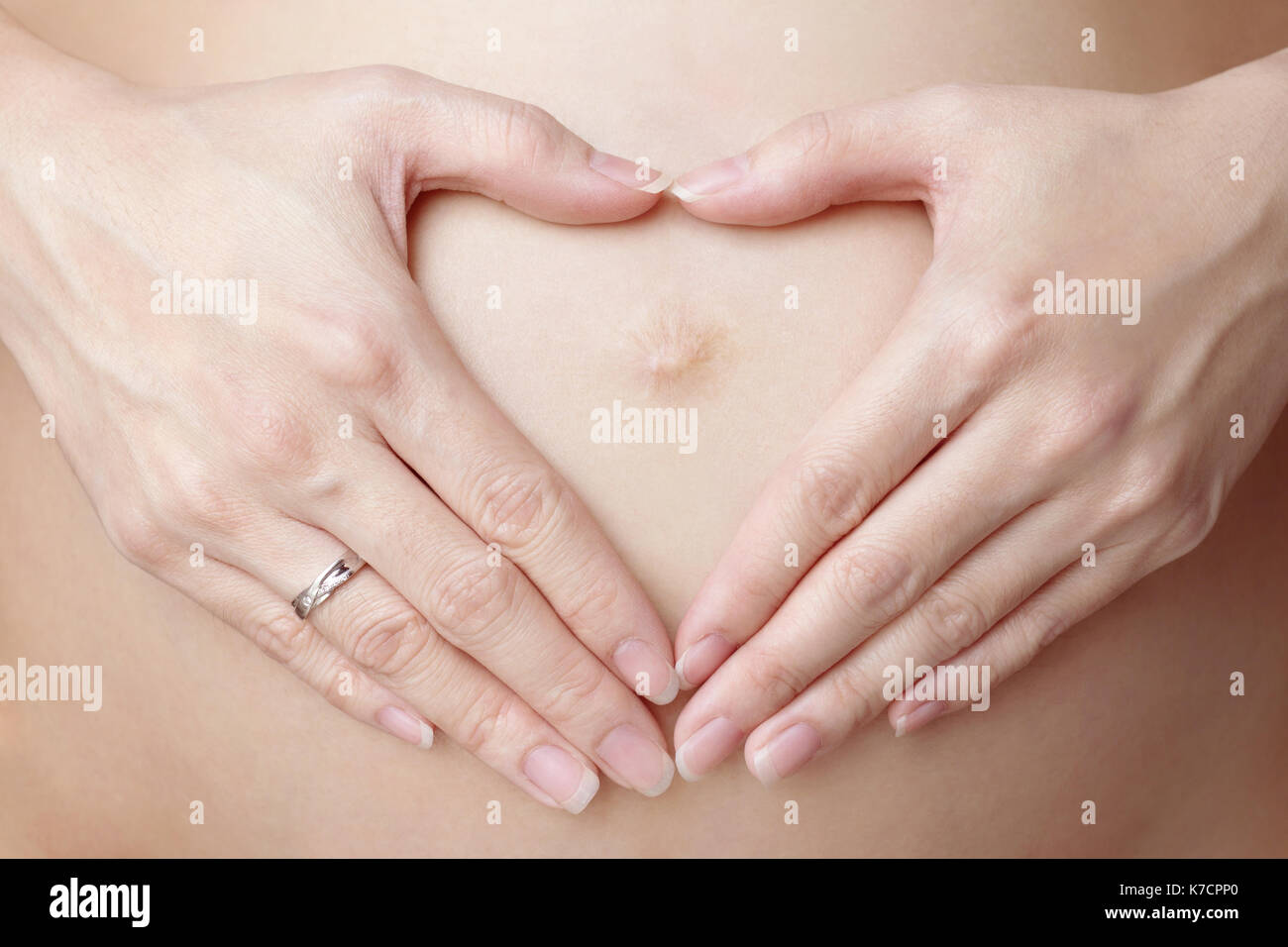 Donna che mantiene le sue mani a forma di cuore sul suo ventre in gravidanza Foto Stock