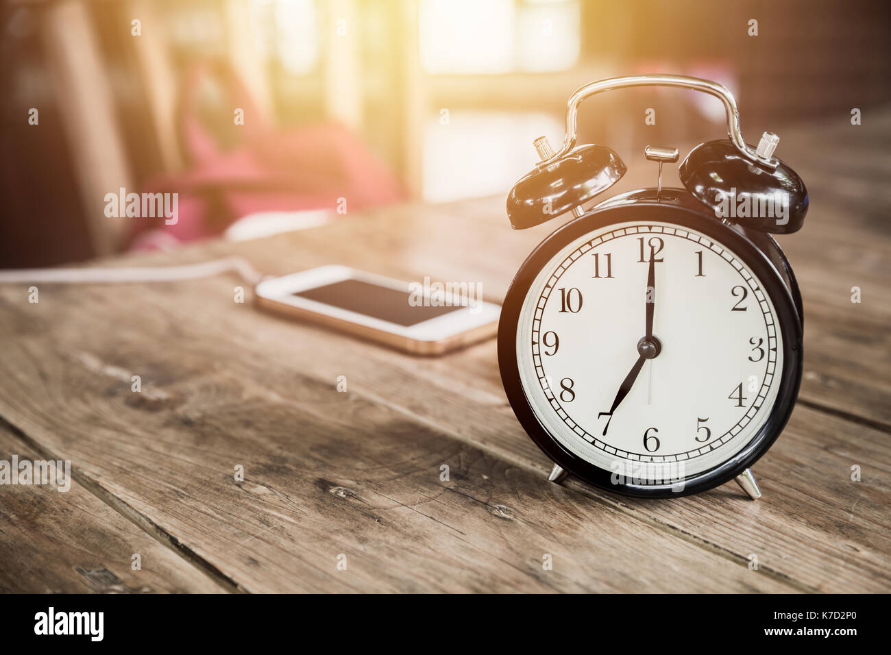 Tempi di clock a 7 ore di mattina sulla tavola di legno con smart phone carica presso il cafe la sfocatura dello sfondo. Foto Stock