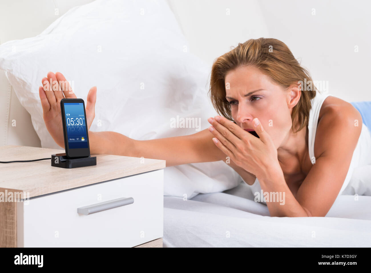 Giovane donna a sbadigliare mentre la funzione snooze allarme sul telefono cellulare Foto Stock