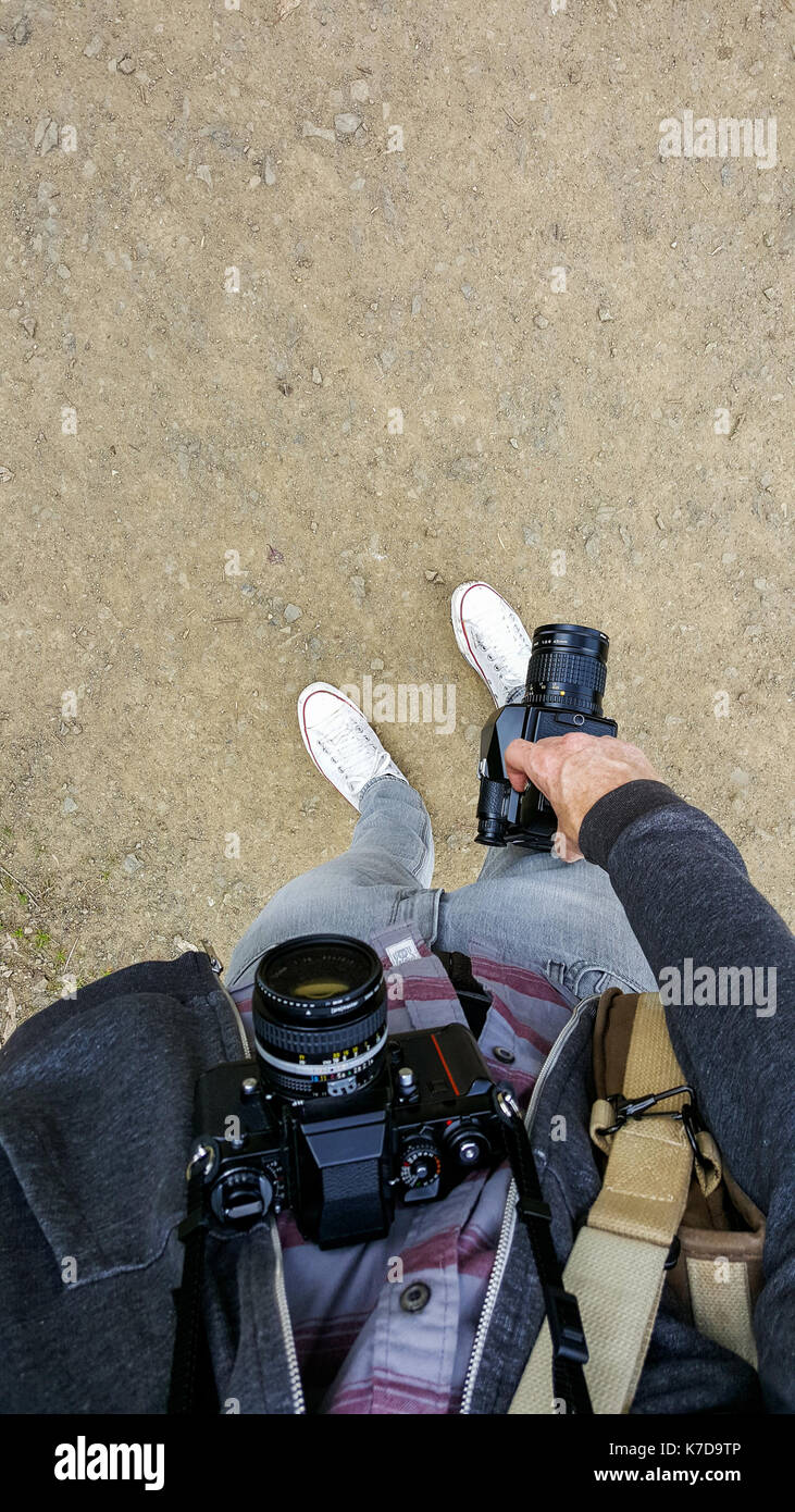 Sezione bassa dell'uomo tenendo la fotocamera digitale mentre si sta in piedi sul terreno Foto Stock