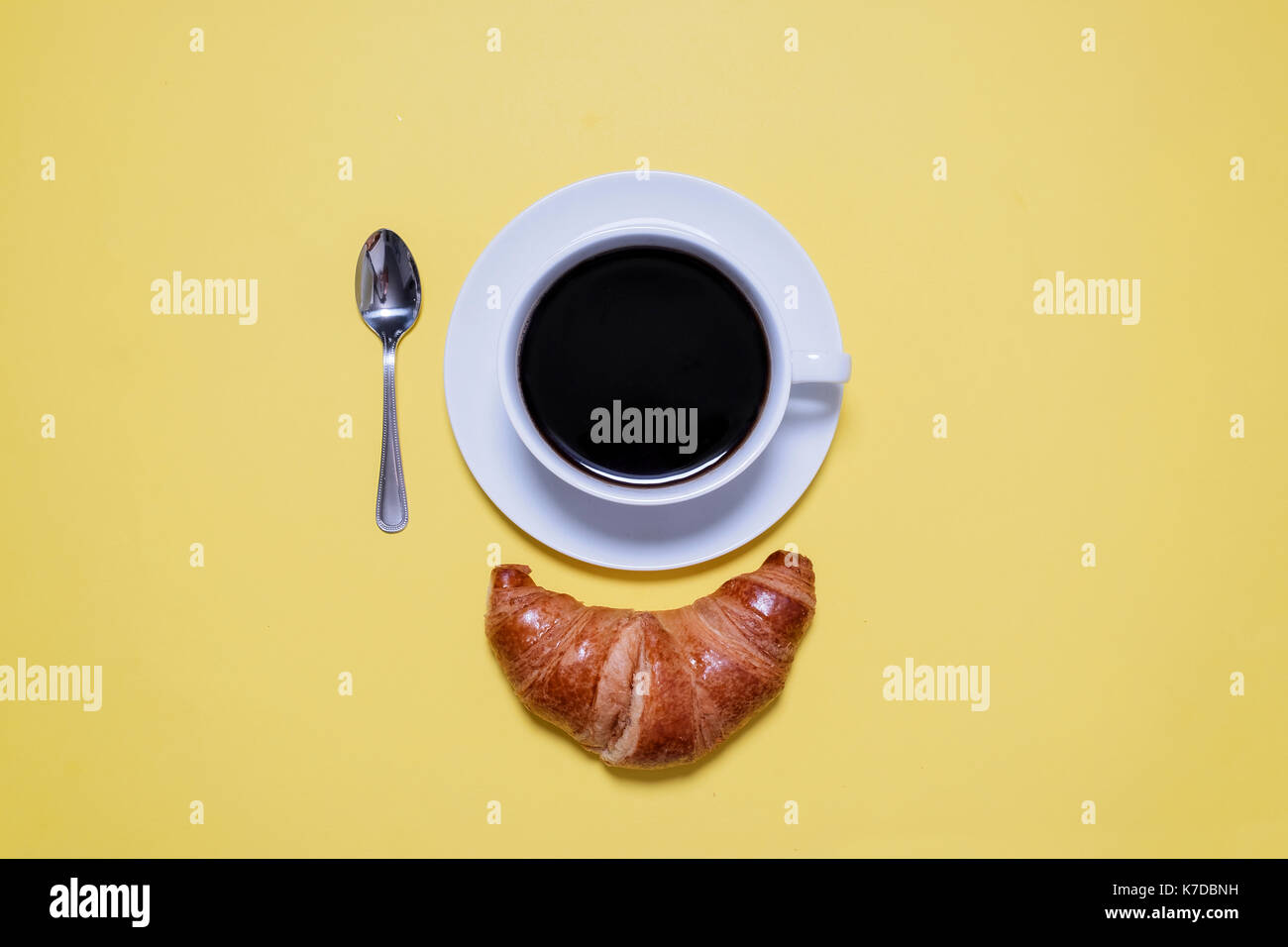 Vista aerea di caffè nero, cucchiaio e croissant sulla tabella di colore giallo Foto Stock