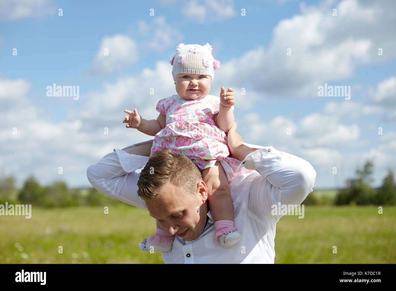 Ritratto di simpatici baby ragazza seduta sul padre di spallamento in campo contro il cielo durante la giornata di sole Foto Stock