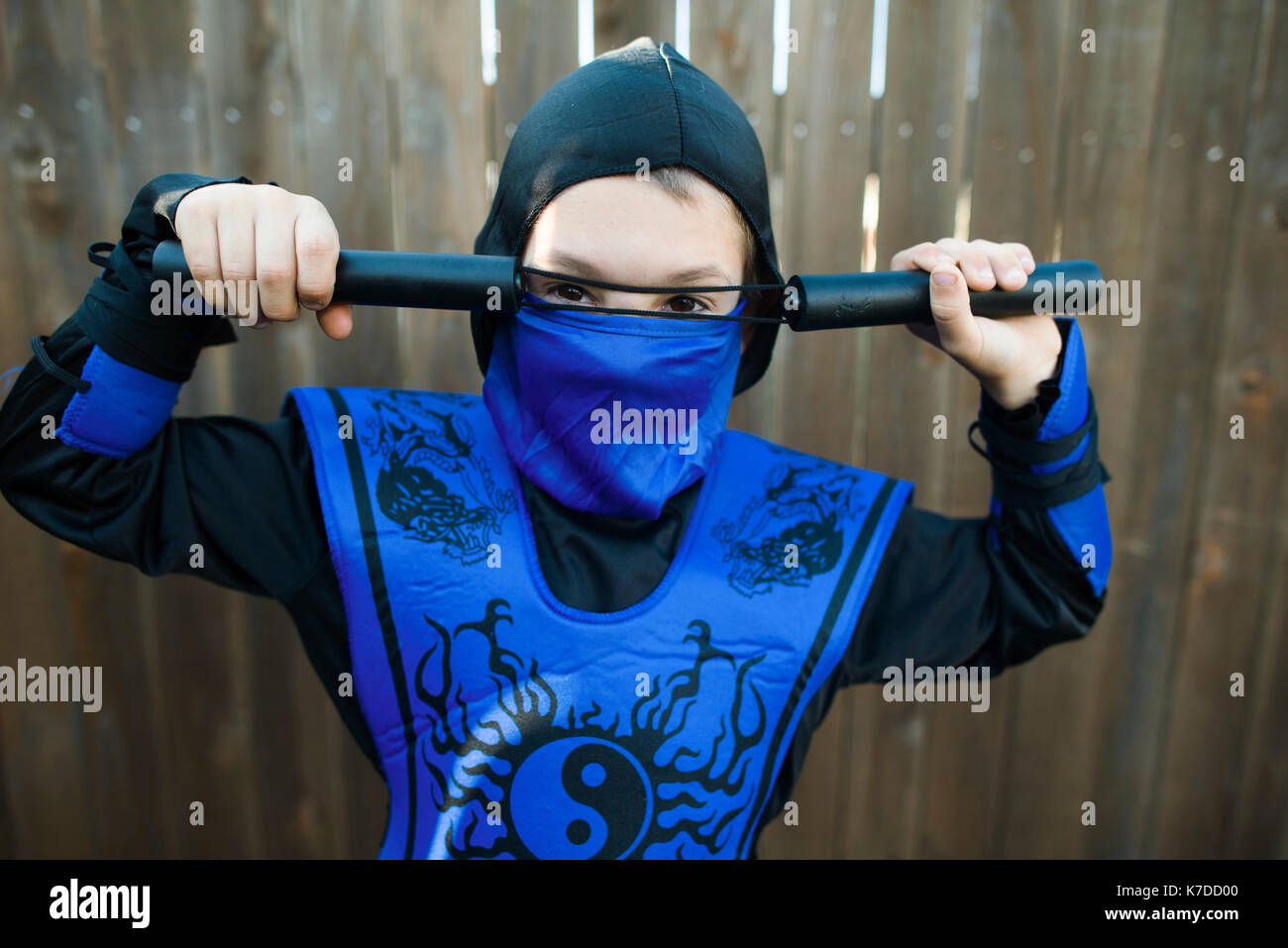 Ritratto di ragazzo in costume ninja in piedi contro la recinzione di legno Foto Stock