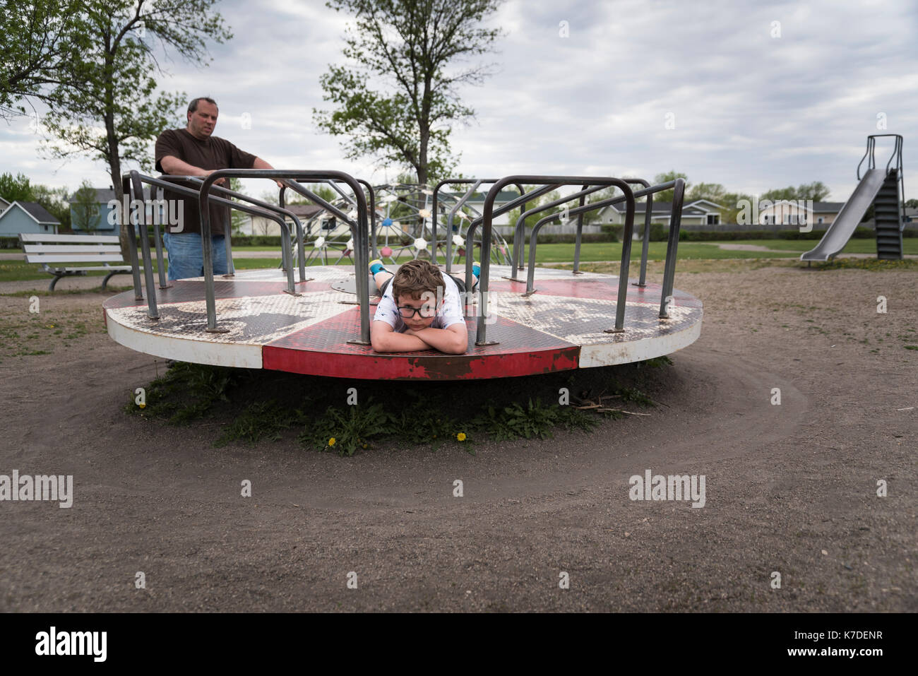 Padre guardando il figlio giacente su merry-go-round al parco giochi Foto Stock
