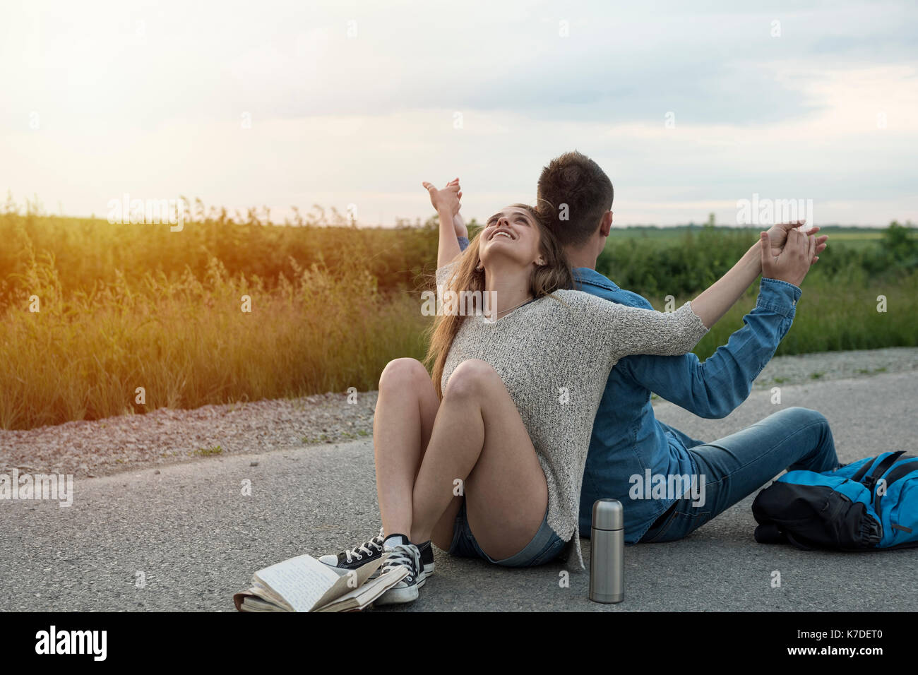 Giovani escursionismo coppia tenendo le mani durante la seduta di schiena su strada di campagna contro sky Foto Stock