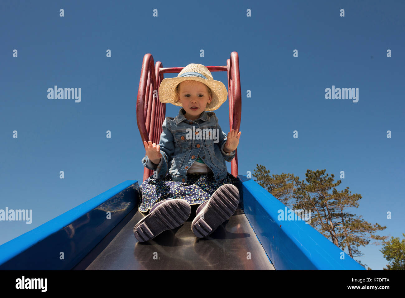 Basso angolo di visione od carina ragazza che gioca sulla slitta al parco giochi contro il cielo chiaro Foto Stock