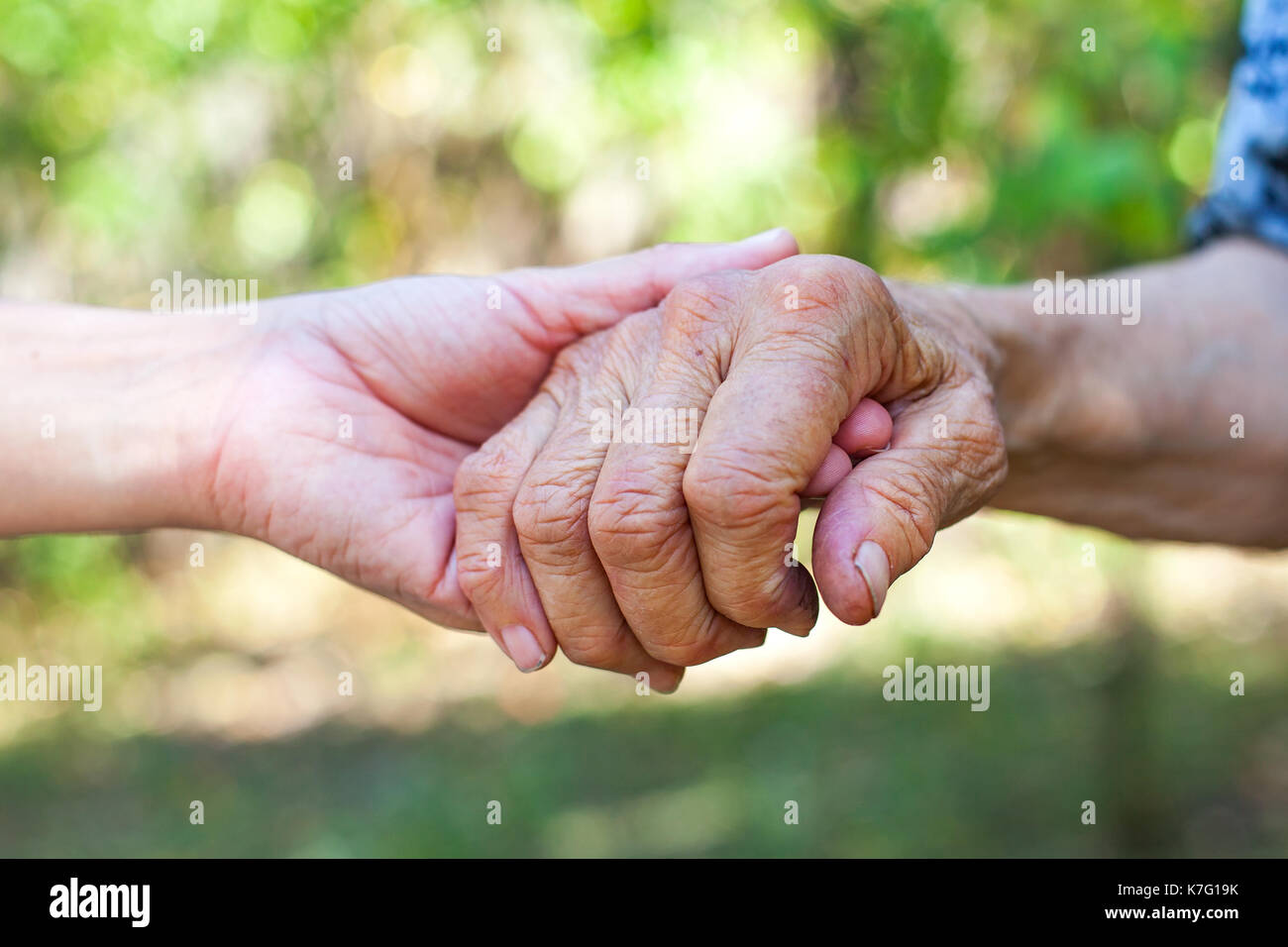 Chiudere fino agli anziani della femmina agitando a mano dal giovane badante con le mani in mano all'aperto Foto Stock