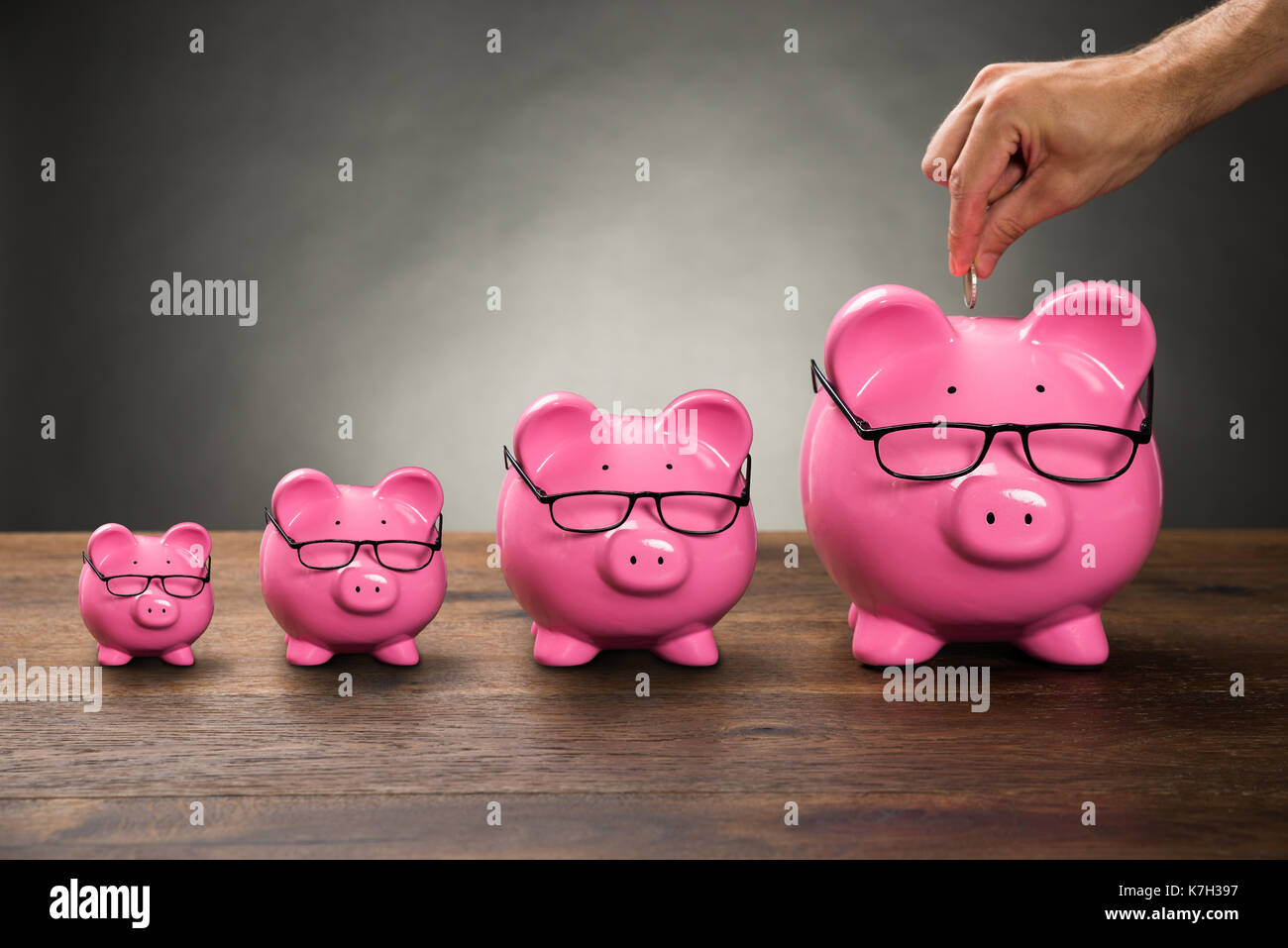 Close-up di persona lato inserimento di moneta in rosa piggybank sul tavolo Foto Stock