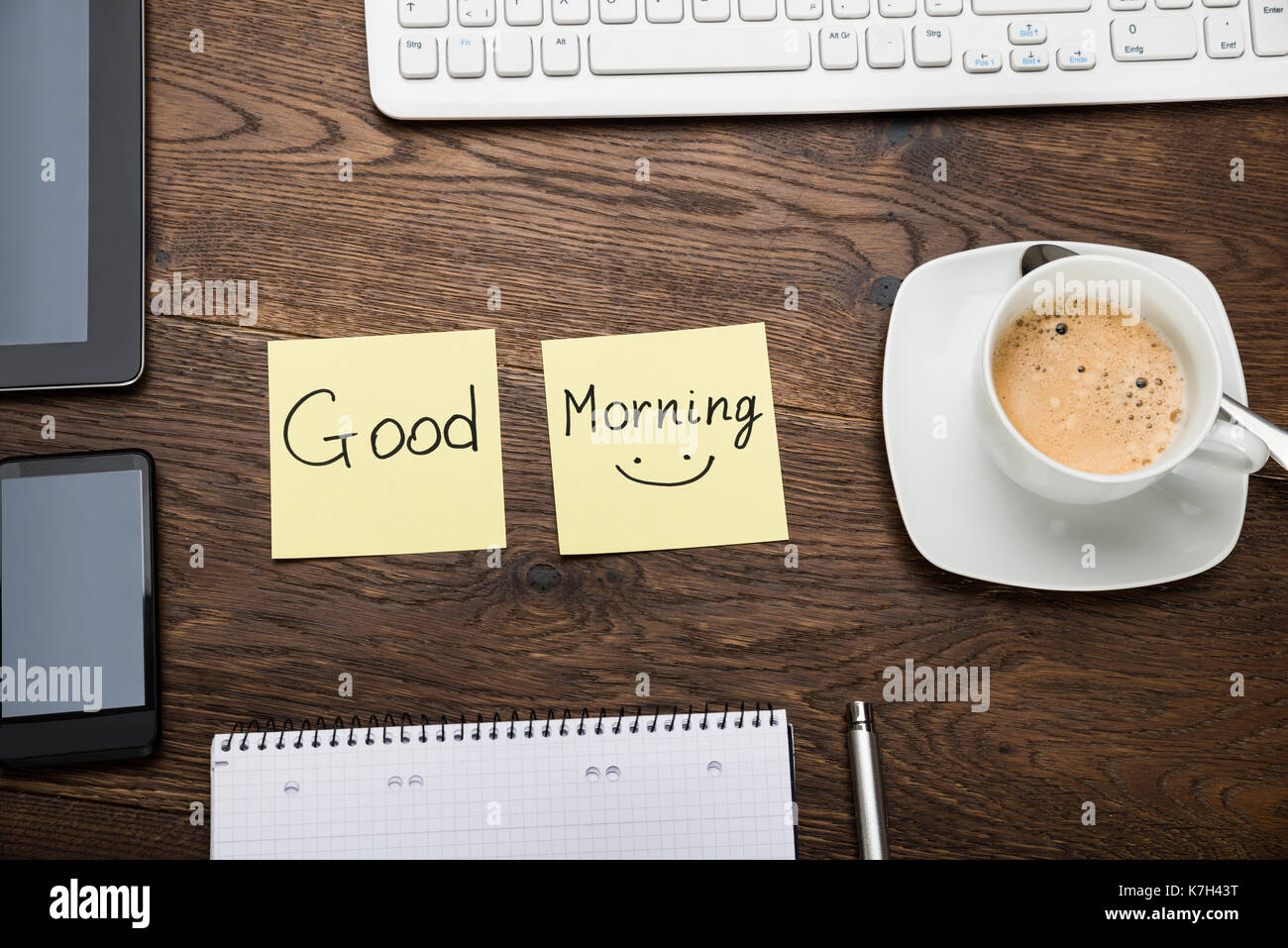Il testo di buona mattina sulla nota adesiva con tazza di caffè sulla scrivania in legno Foto Stock