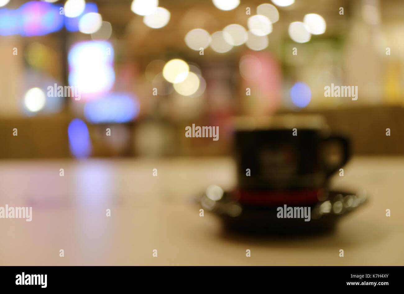 Immagine sfocata di una tazza di una bevanda calda sul tavolo di legno nel coffee shop con luci bokeh di fondo Foto Stock