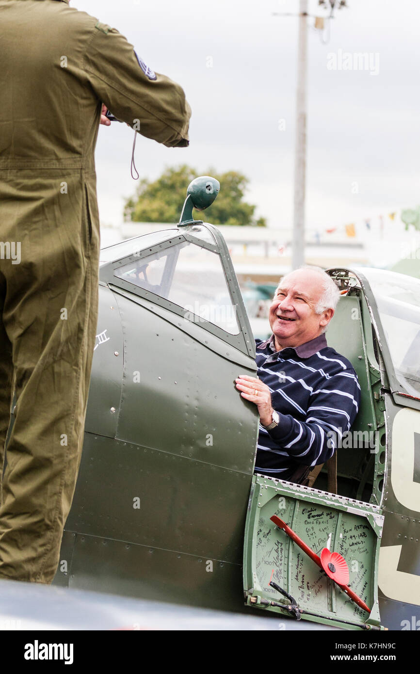 Inghilterra, Chatham Dockyard. Evento, salutare per gli anni quaranta. Uomo anziano, sorridenti mentre è seduto nella cabina di pilotaggio di uno Spitfire guerra mondiale due fighter e in posa per una fotografia. Foto Stock