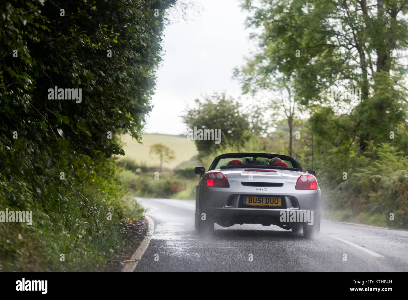 Un automobilista alla guida della sua open-top (cabriolet) car sotto la pioggia lungo la B4340 in Galles Foto Stock