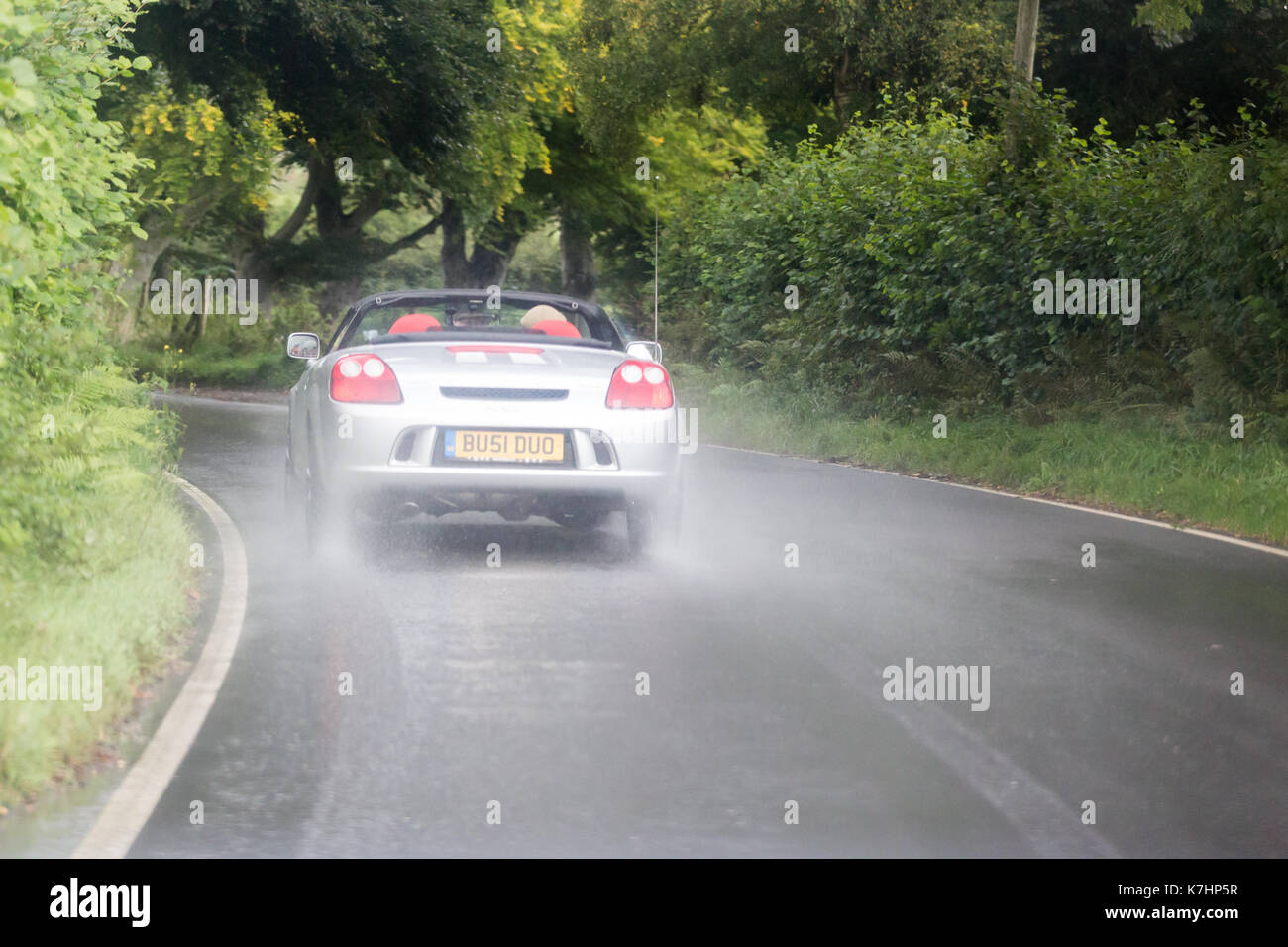 Un automobilista alla guida della sua open-top (cabriolet) car sotto la pioggia lungo la B4340 in Galles Foto Stock