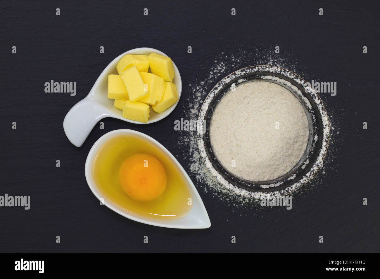 Il concetto di cibo di base forno ingredienti farina, uova e burro in ardesia nera lastra di pietra Foto Stock
