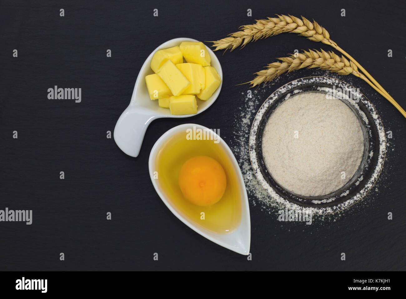 Il concetto di cibo di base forno ingredienti farina, uova e burro in ardesia nera lastra di pietra Foto Stock