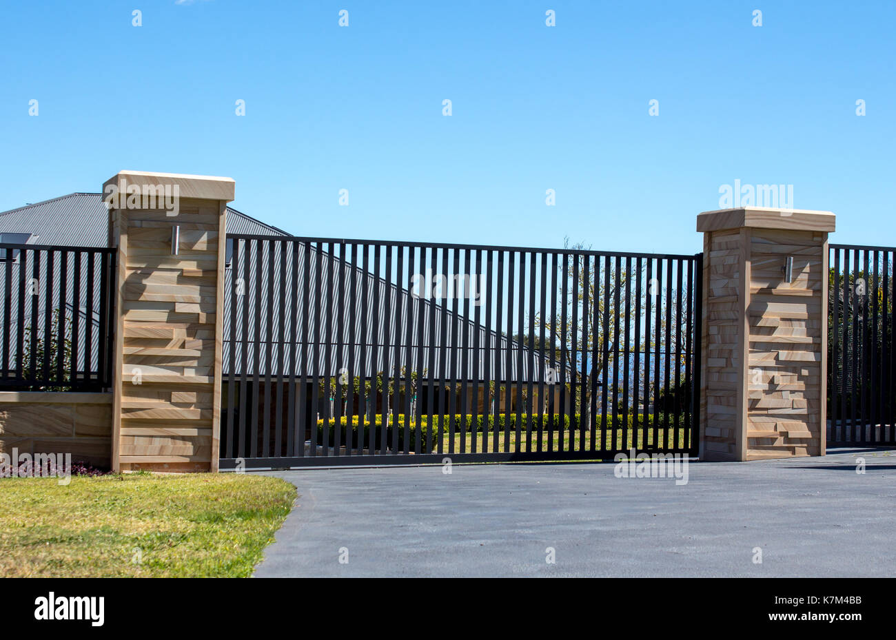 Metallo nero carraio cancelli di ingresso impostato in arenaria di recinzione in mattoni con giardino residenziale in background Foto Stock