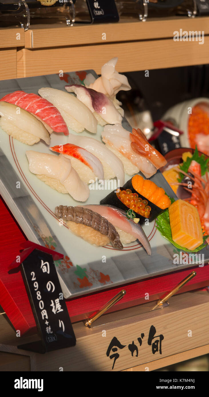 Plastica display sushi al ristorante la finestra con il giapponese nero e rosso segno bianco con scritte e informazioni sul prezzo. più tardi pomeriggio di sole caldo e Foto Stock