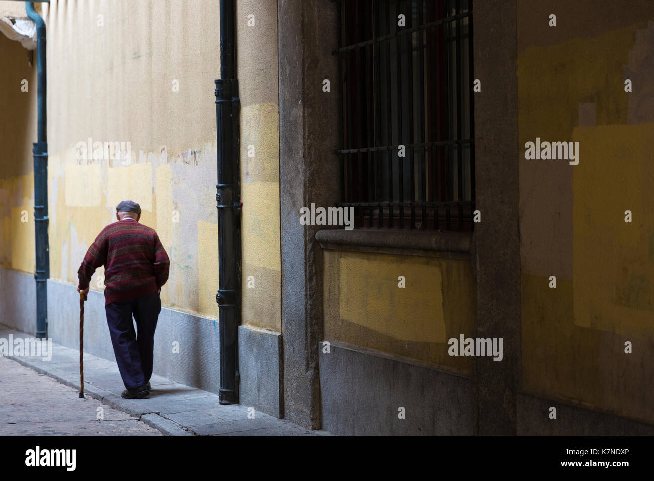 Il vecchio uomo con pochi ammalati e indossando il cappuccio a passeggiare nella città vecchia Avila, Spagna Foto Stock