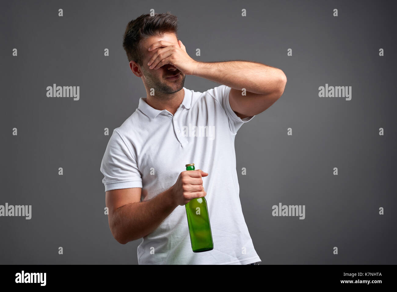 Un bel giovane sensazione disperata e afferrando la sua testa mentre si tiene una birra Foto Stock