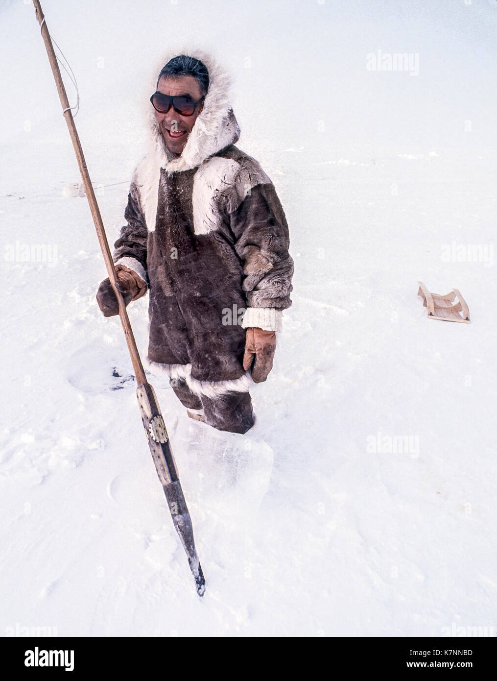 Inuit uomo anziano, metà 60s, vestito di Caribou Coffee Company tradizionale abbigliamento di pelle, pone con lo strumento che egli utilizza per il taglio di blocchi di ghiaccio per costruire igloo. Foto Stock