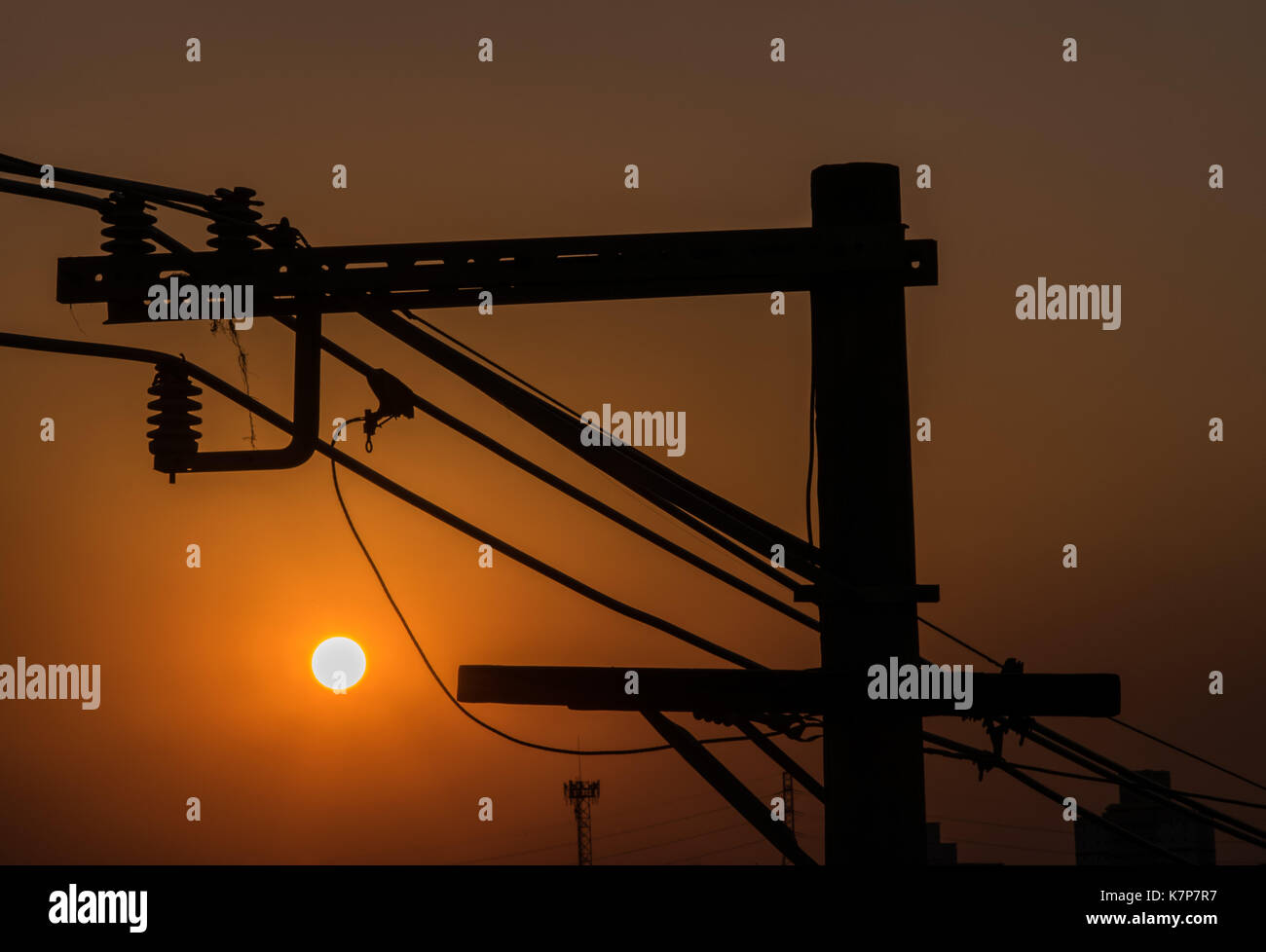 Città di energia elettrica post pole durante il tramonto con cielo arancione e sun in background, silhouette Foto Stock