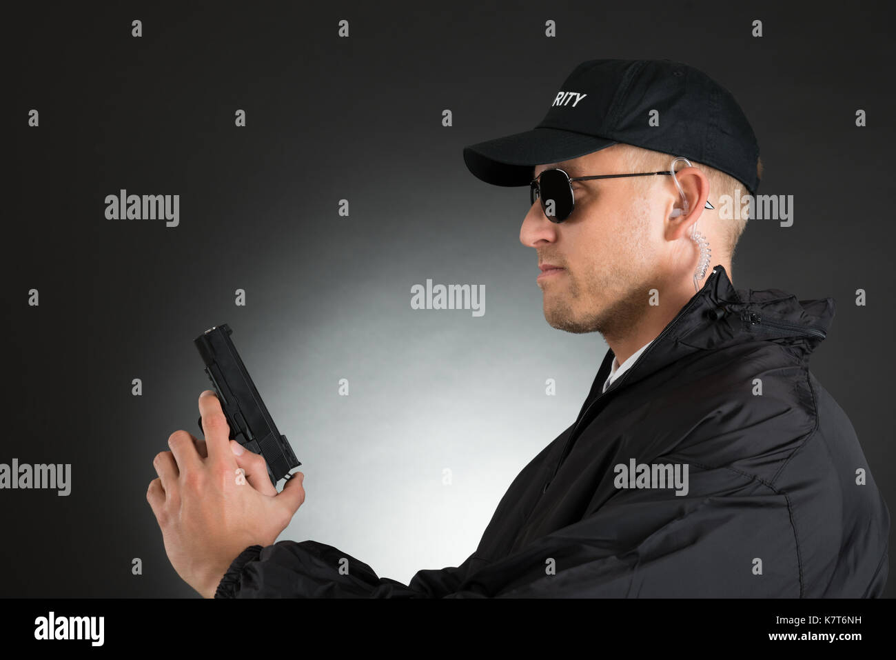 Ritratto di giovane bodyguard tenendo la pistola su sfondo nero Foto Stock