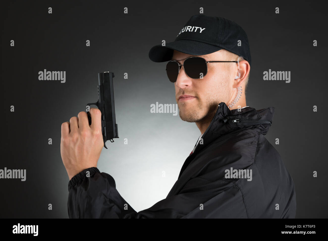 Ritratto di giovane bodyguard tenendo la pistola su sfondo nero Foto Stock
