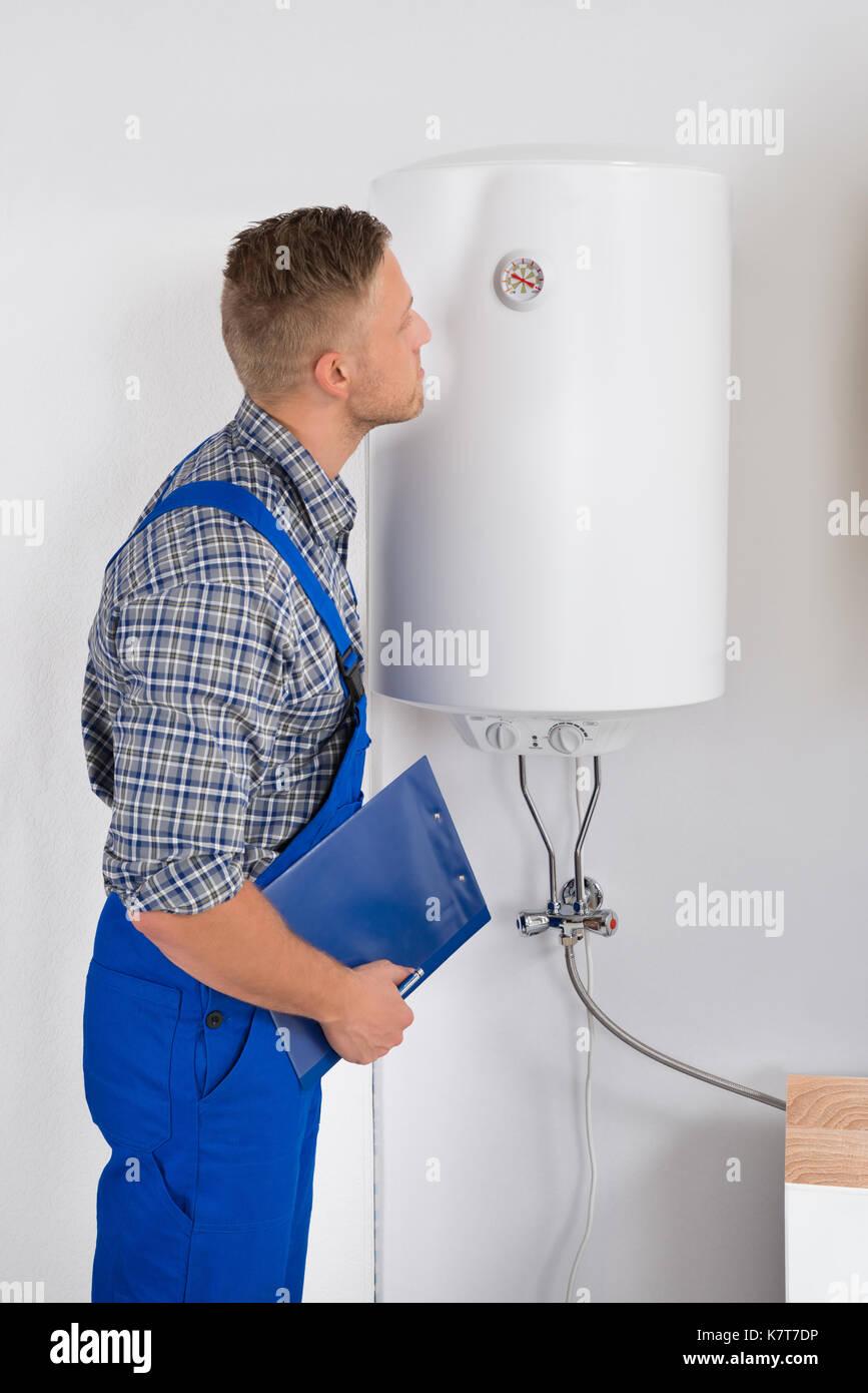 Giovane maschio aggiustatore con appunti guardando il comparatore sulla caldaia elettrica Foto Stock