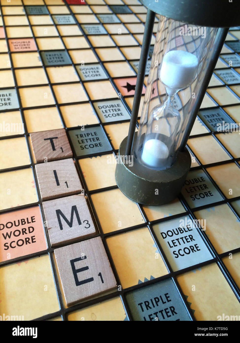 La parola 'tempo' enunciato su un gioco SCRABBLE board, accanto a una clessidra Foto Stock