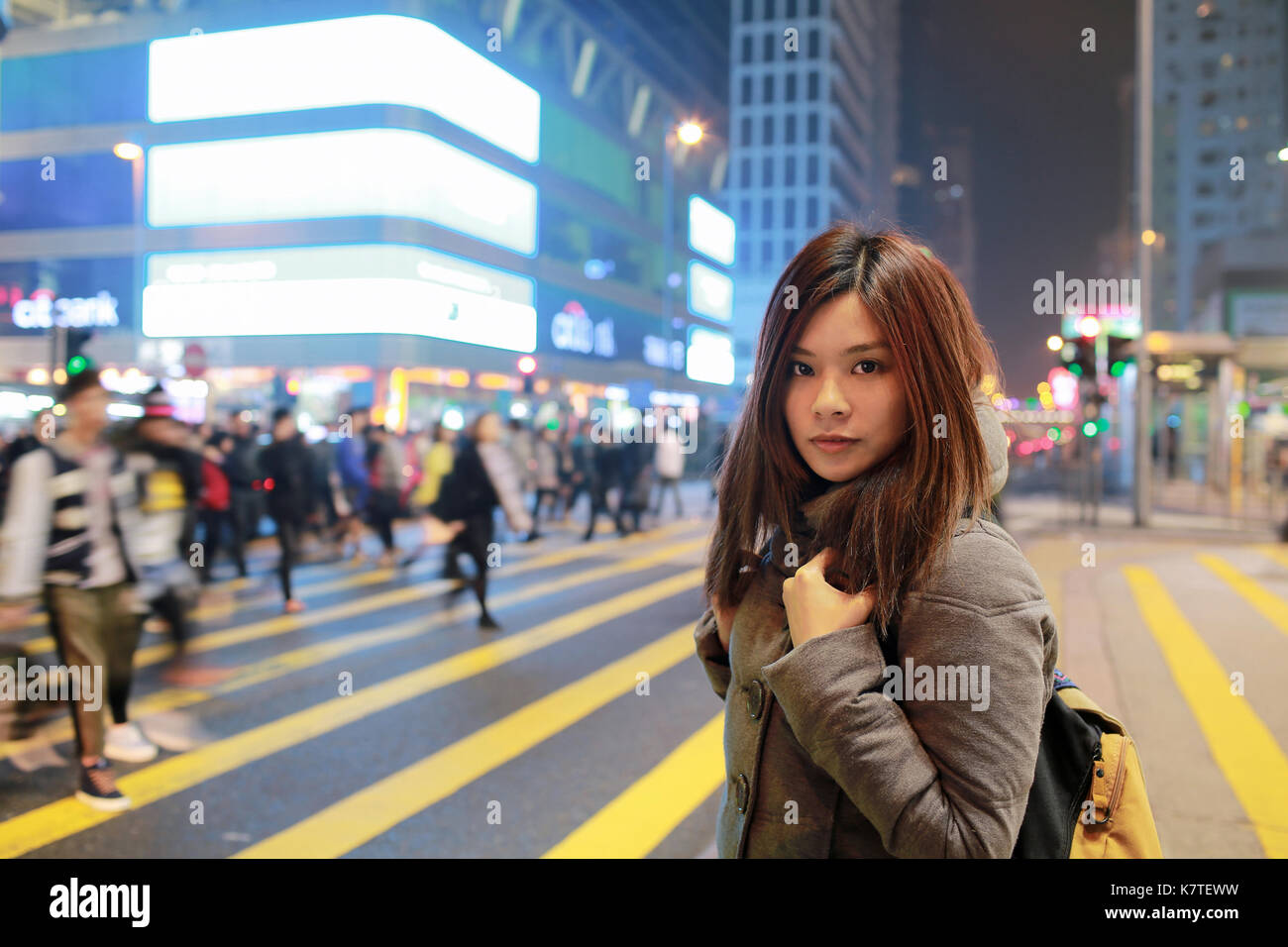 Giovane e bella ragazza stare fuori e guardare in notturna a Hong kong, perso in città , Occupato folla e giallo zebra crossing sfondo sfocato Foto Stock
