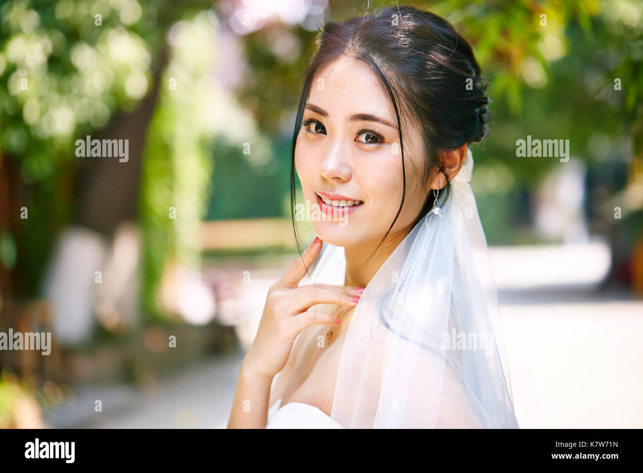 Outdoor ritratto della bella e felice di giovani asiatici sposa indossa velo nuziale. Foto Stock