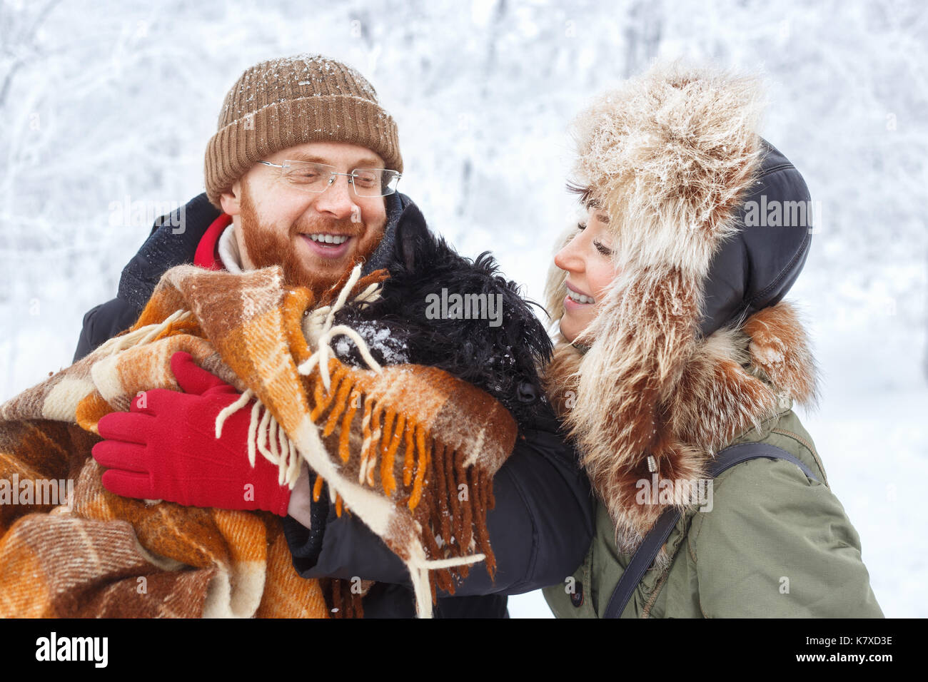 Ritratto di felice inverno giovane con pet piccolo cane scottish terrier. giovane uomo e donna in amore con il cane a piedi nei boschi innevati. famiglia giocando Foto Stock