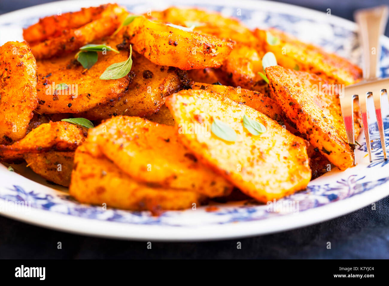 Fettine rotonde patate al forno con condimenti piccanti e foglie di erbe Foto Stock