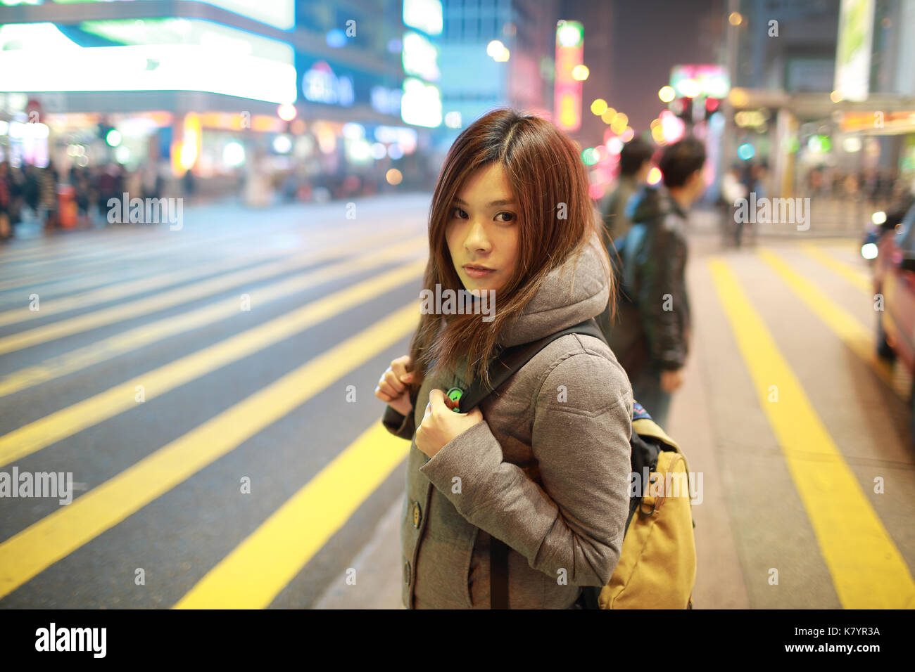 Giovane e bella ragazza stare fuori e guardare in notturna a Hong kong, perso in città , Occupato folla e giallo zebra crossing sfondo sfocato Foto Stock