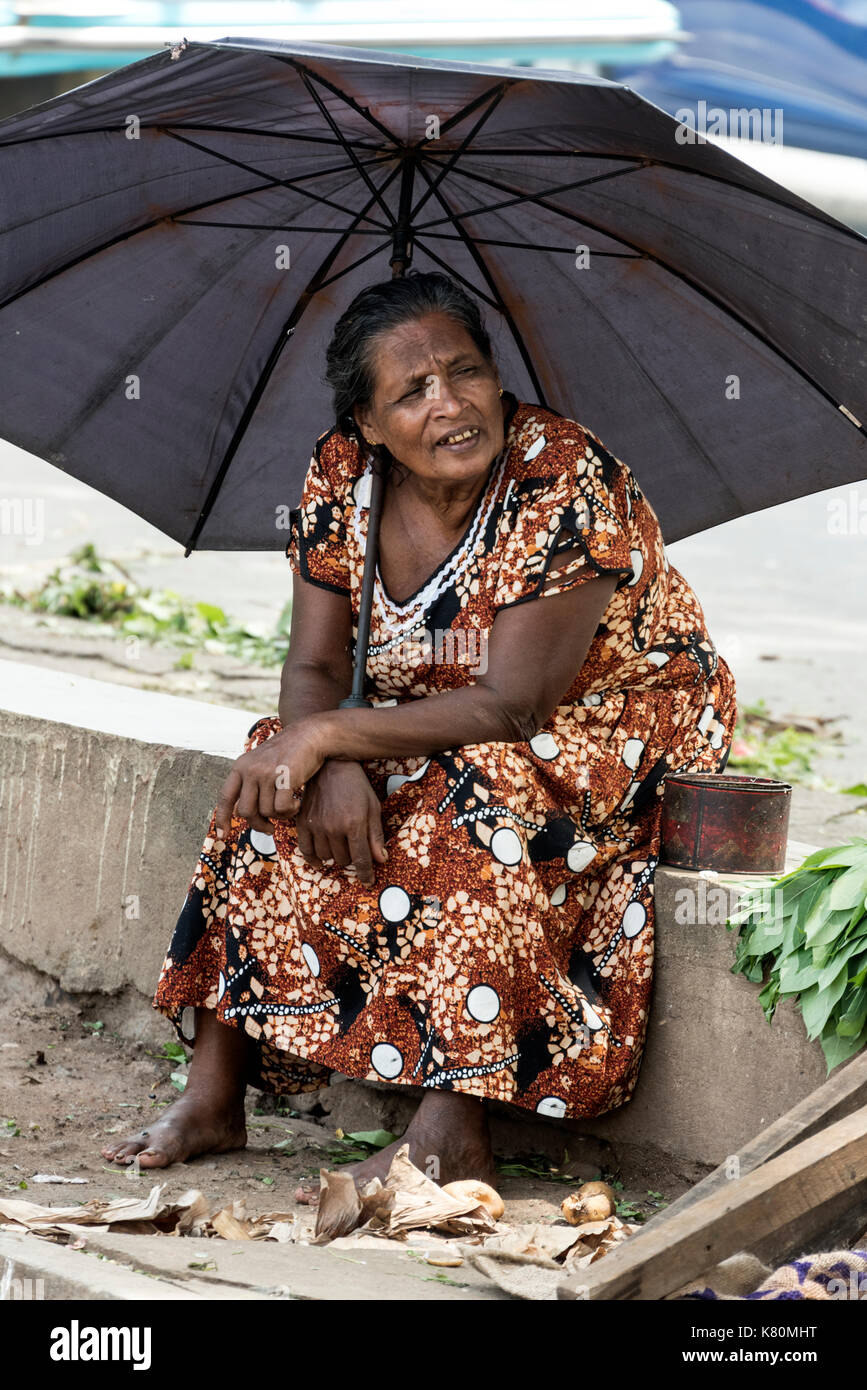 Un dello Sri lanka la donna con il suo ombrello dal calore del giorno, in corrispondenza di una piccola produzione fresca mercato accanto a una strada principale molto trafficata in Colombo, Sri lanka Foto Stock