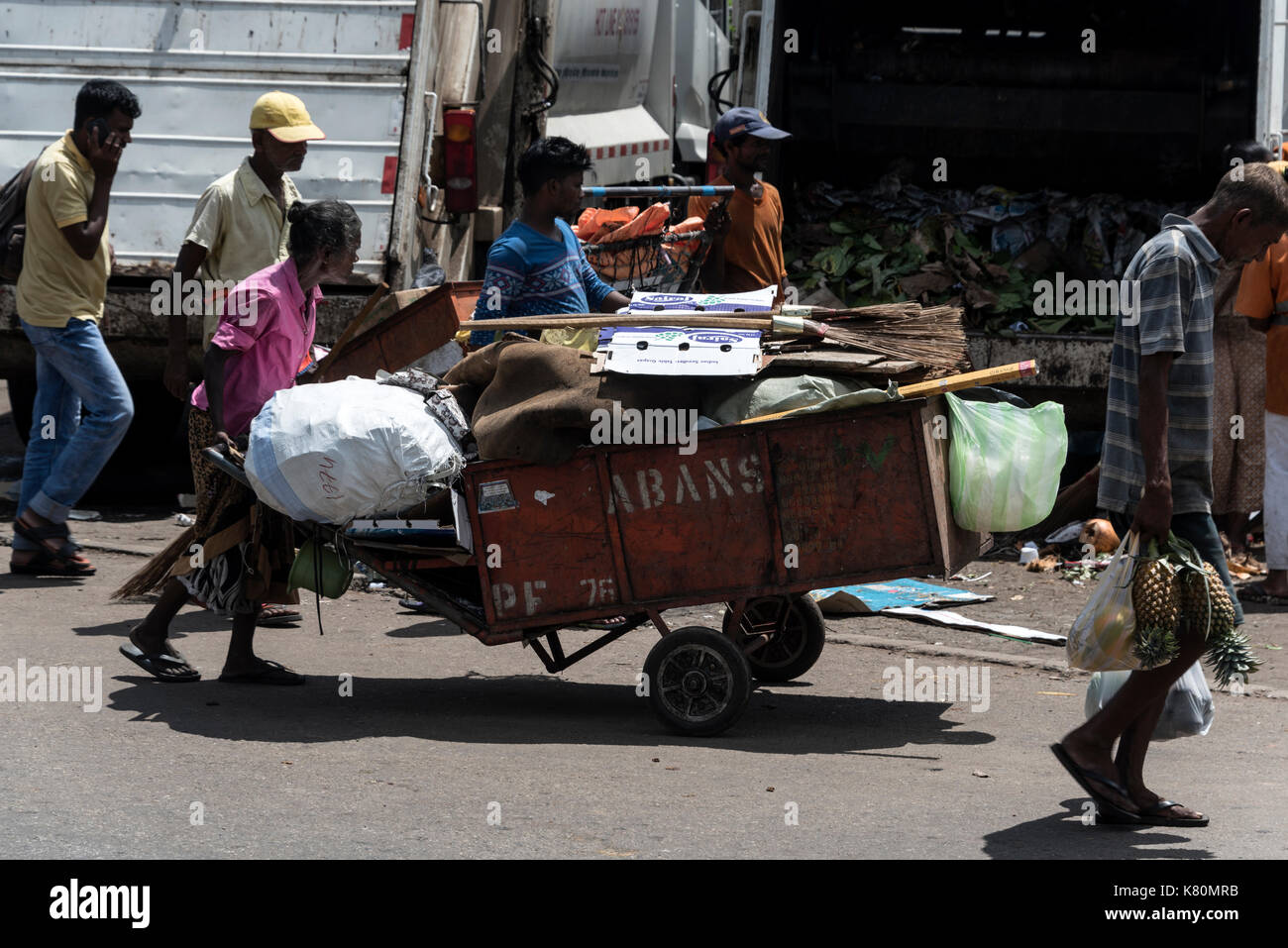 Una donna che spinge la ruota barrow di spazzatura, ( garbage) lungo una strada trafficata in pettah distretto di Colombo, Sri lanka Foto Stock