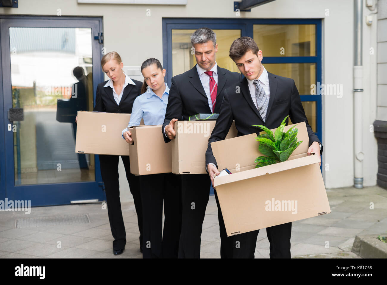 Deluso gli imprenditori in piedi in fila con scatole di cartone al di fuori dell'ufficio Foto Stock