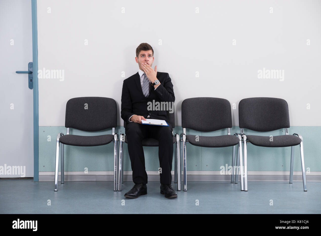 Giovane imprenditore tenendo negli appunti e sbadigli mentre è seduto su una sedia Foto Stock