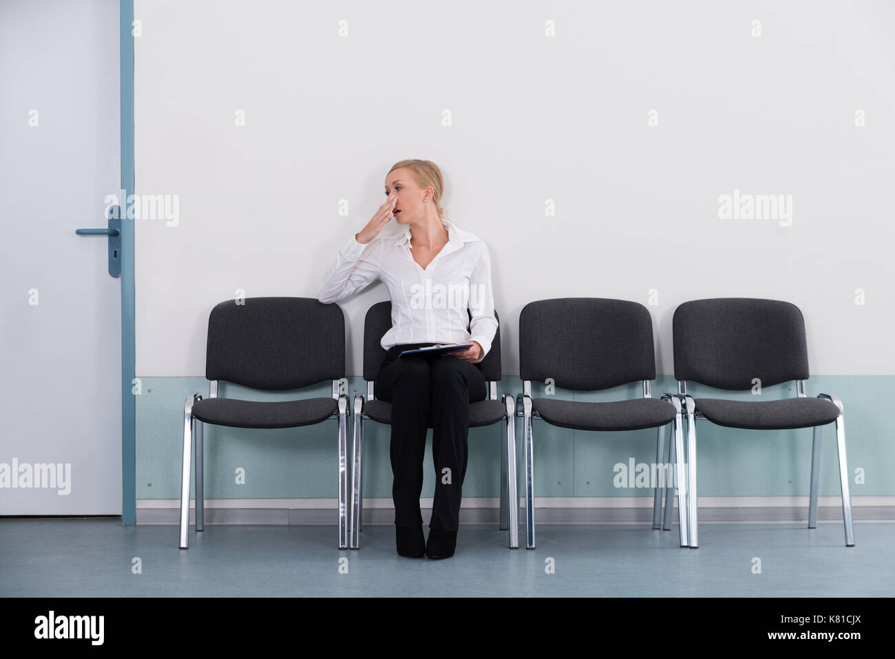 Annoiato giovane imprenditrice sbadigliare mentre è seduto su una sedia in ufficio Foto Stock
