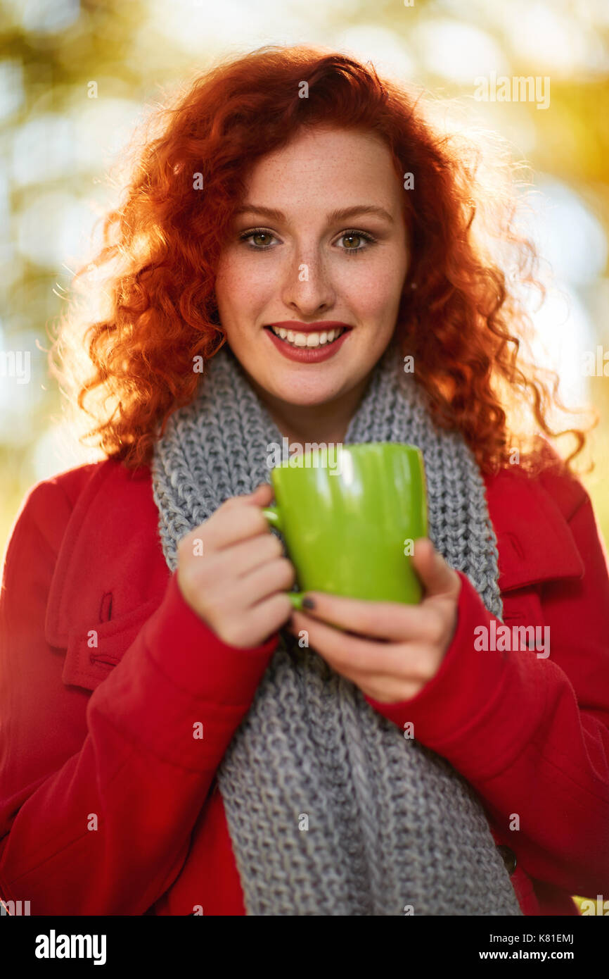Lo zenzero carina ragazza con tazza verde nella natura Foto Stock