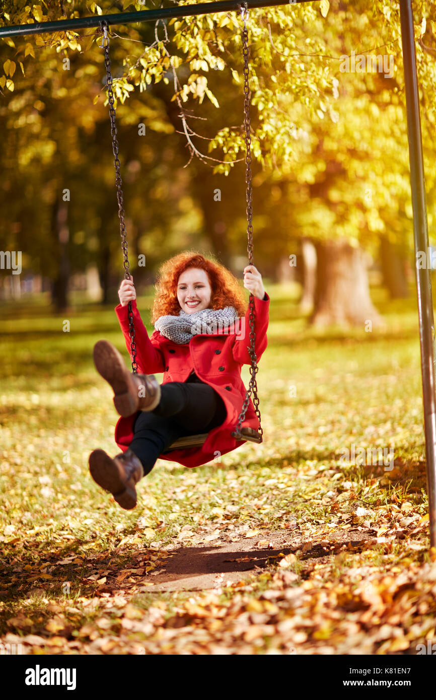 Redhead oscillanti femmina su un altalena nel parco in autunno Foto Stock