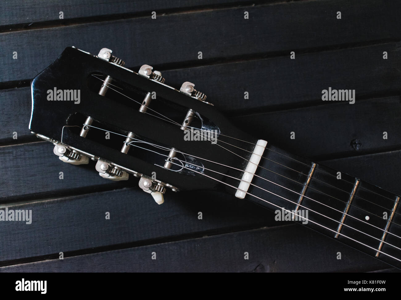 Nero chitarra acustica di testa, piroli, dado e stringhe, su di un legno nero lo sfondo della tabella, con un sacco di texture di sfondo e linee Foto Stock