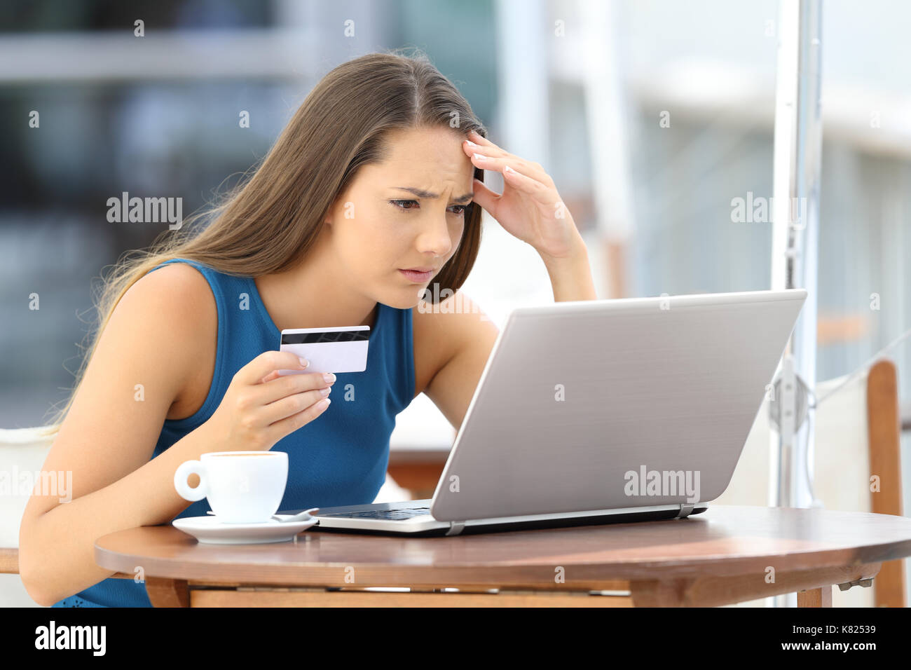 Preoccupati sulla linea shopper cerca di pagare con una carta di credito e un laptop seduto in un bar terrazza Foto Stock