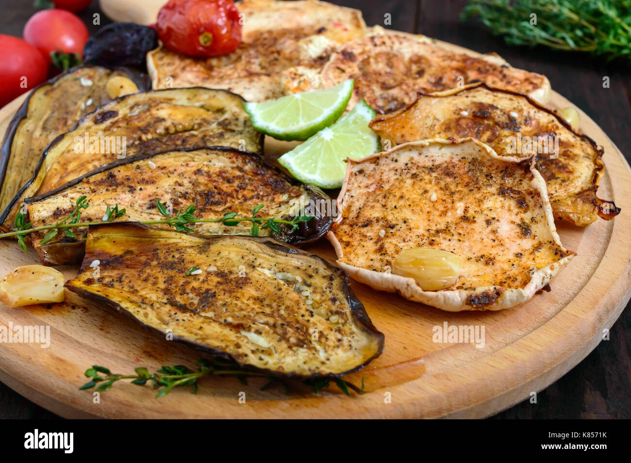 Verdure al forno: melanzane, patisson, pomodori in un giro di supporto di legno su uno sfondo scuro. piatto vegano. Foto Stock
