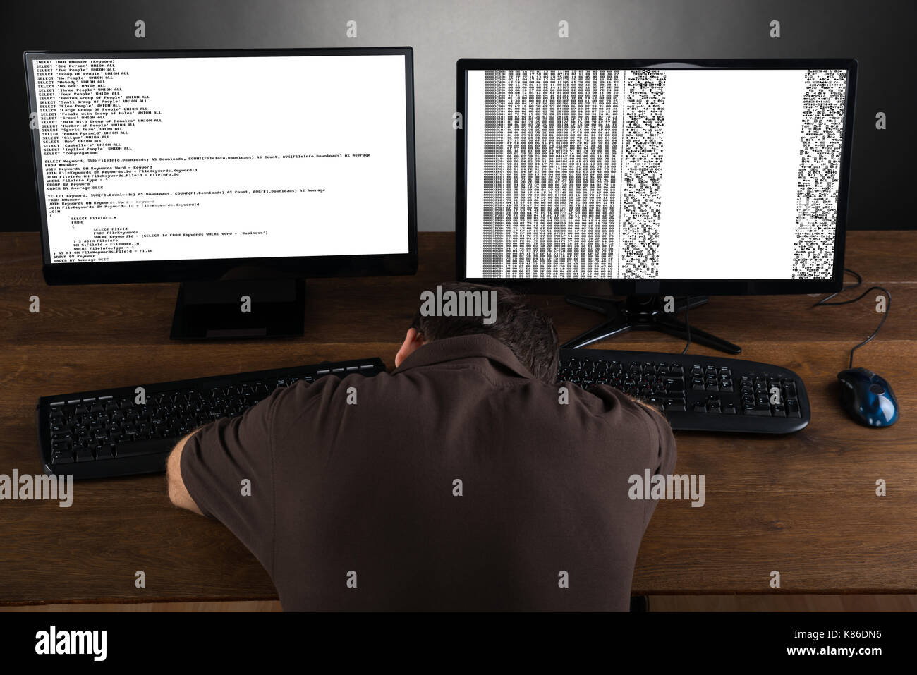 Uomo dorme da scrivania con computer che mostra il codice di un programma Foto Stock