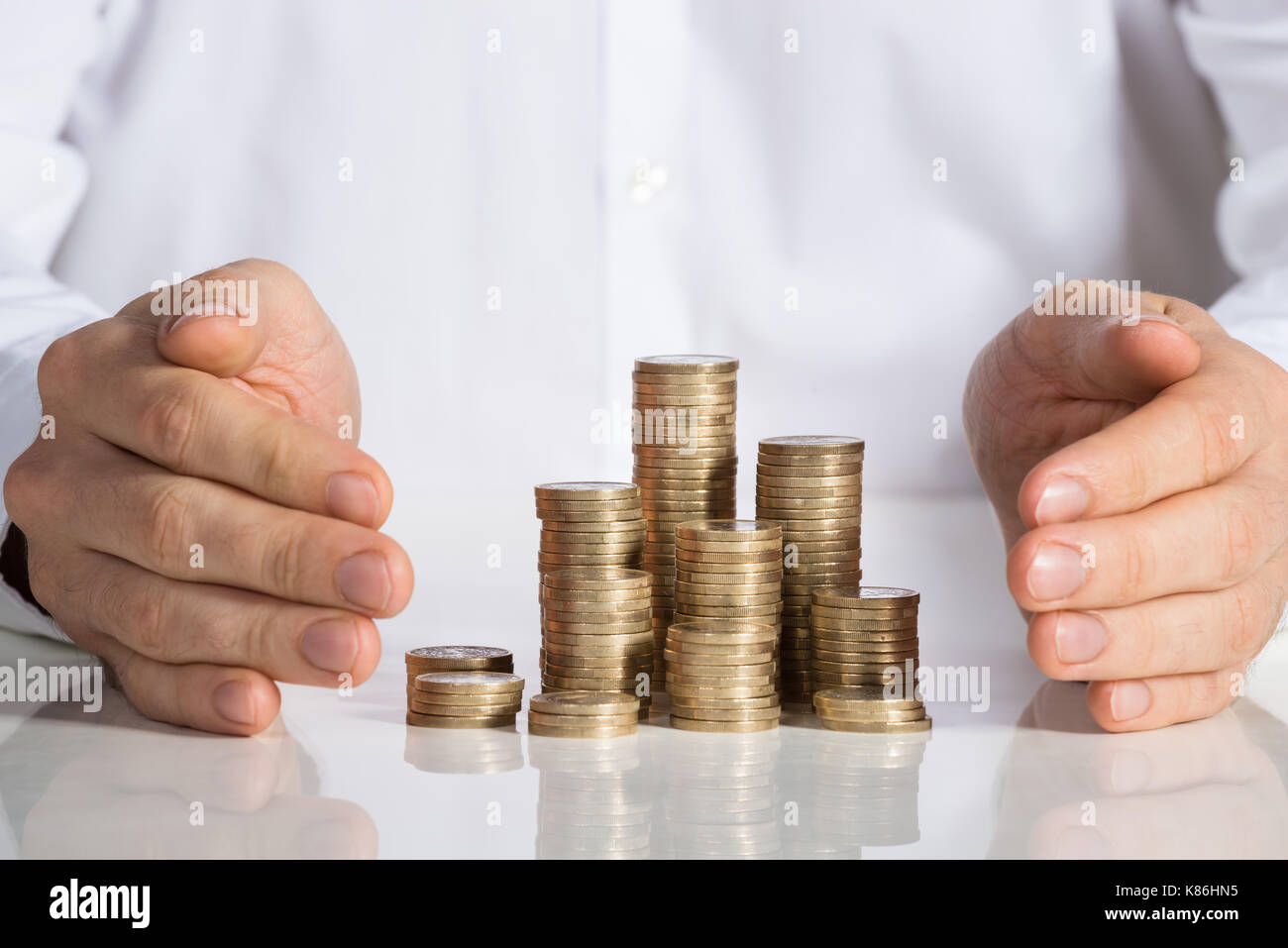 Sezione mediana di imprenditore proteggere le monete impilate a scrivania da ufficio Foto Stock