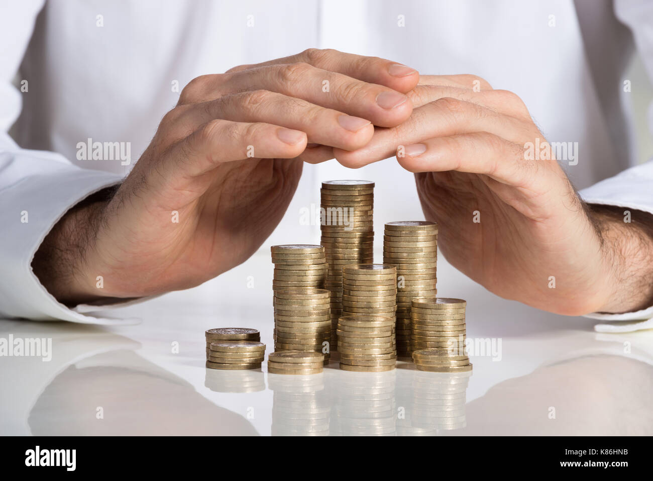 Sezione mediana di imprenditore proteggere le monete impilate a scrivania da ufficio Foto Stock