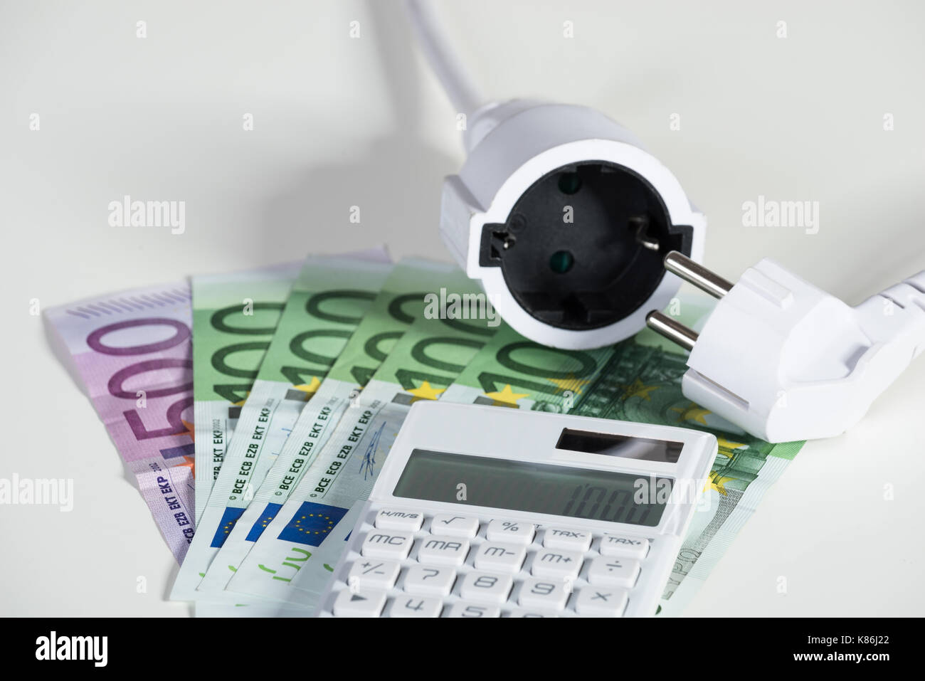 Primo piano della calcolatrice con spina elettrica con le banconote in euro su sfondo bianco Foto Stock
