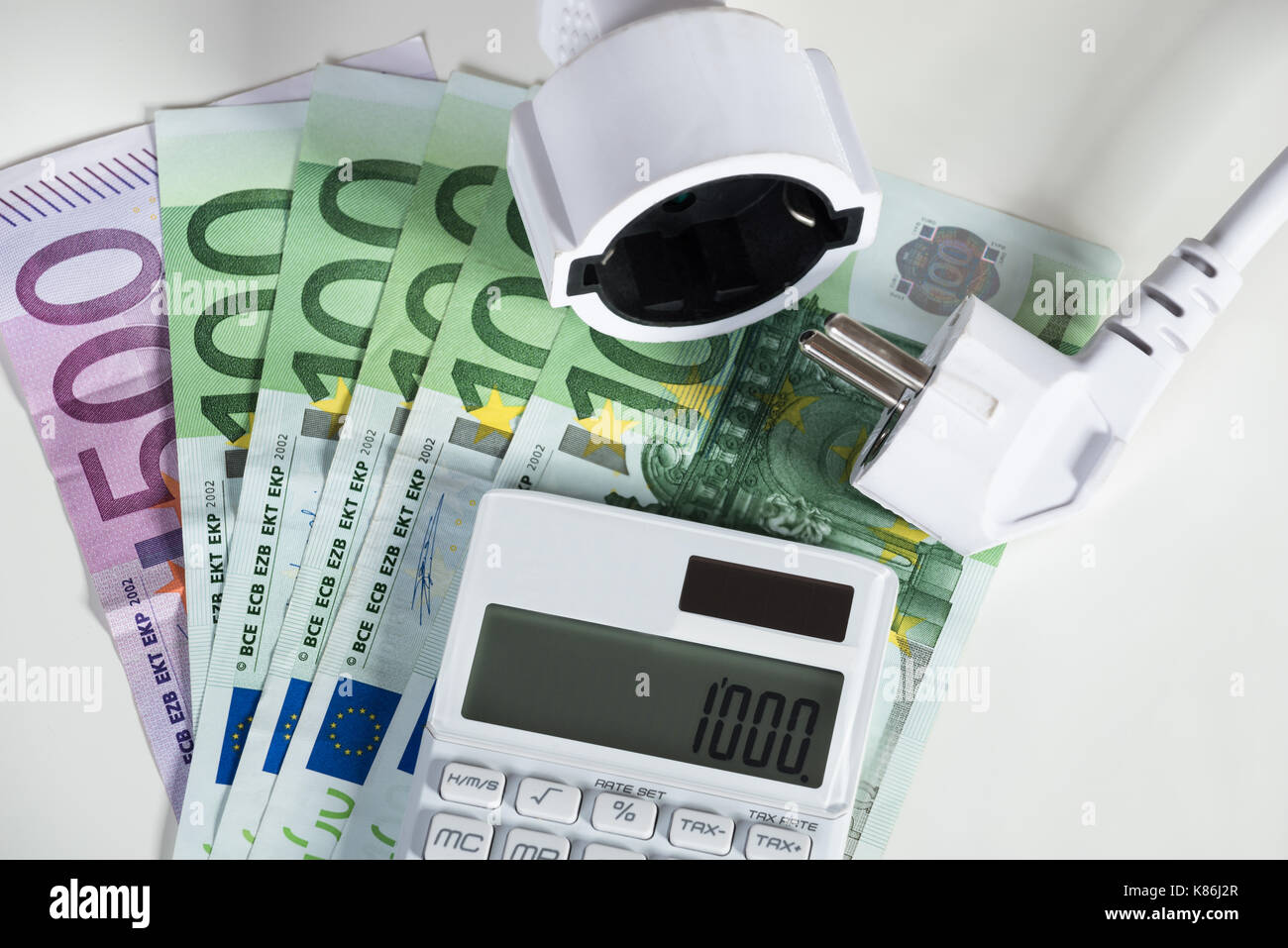 Primo piano della calcolatrice con spina elettrica con le banconote in euro su sfondo bianco Foto Stock
